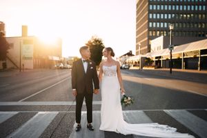 Bride and groom walking together on city street at sunset.