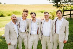 Groomsmen in light beige suits pose together on a sunny outdoor lawn.