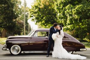 Classic vintage car parked on tree-lined street during sunset wedding photoshoot.