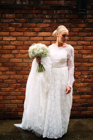 Lace wedding dress detail against rustic brick wall with baby's breath bouquet.