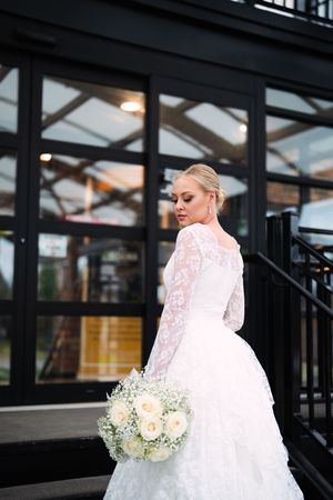 A bride in a white wedding dress with lace details poses elegantly in an industrial-style venue.