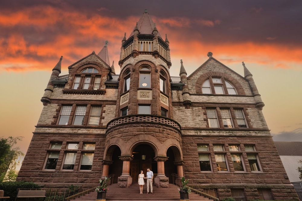 Historic stone castle building with dramatic orange sunset sky behind it.