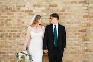 Couple poses against rustic brick wall during wedding photoshoot.
