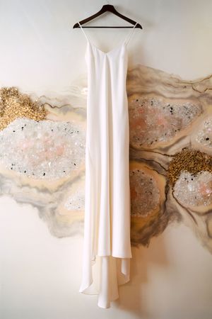 White wedding dress hanging against abstract watercolor wall art with gold accents.