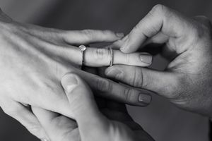 Black and white close-up of hands exchanging wedding rings during ceremony.
