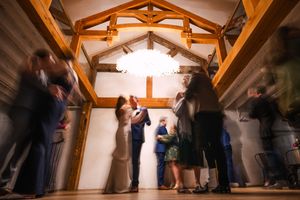 Motion blur captures wedding celebration dancing in rustic timber-framed reception hall.