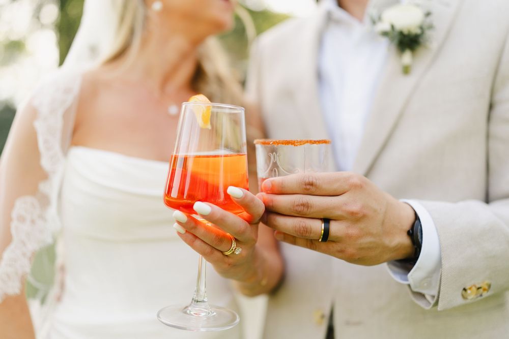Wedding couple toasting with colorful cocktails during outdoor celebration.