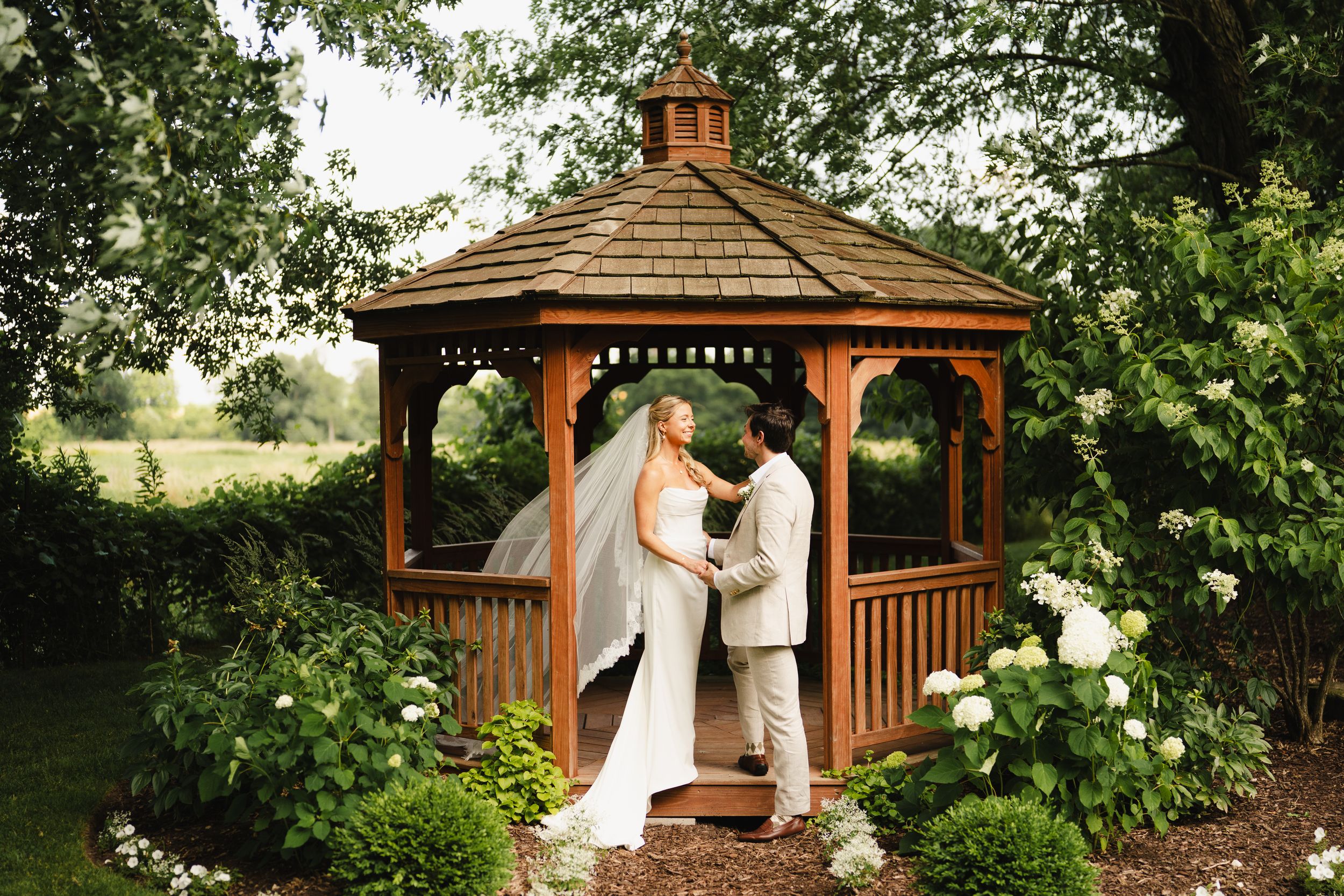 Romantic wedding ceremony moments under a wooden gazebo surrounded by greenery.