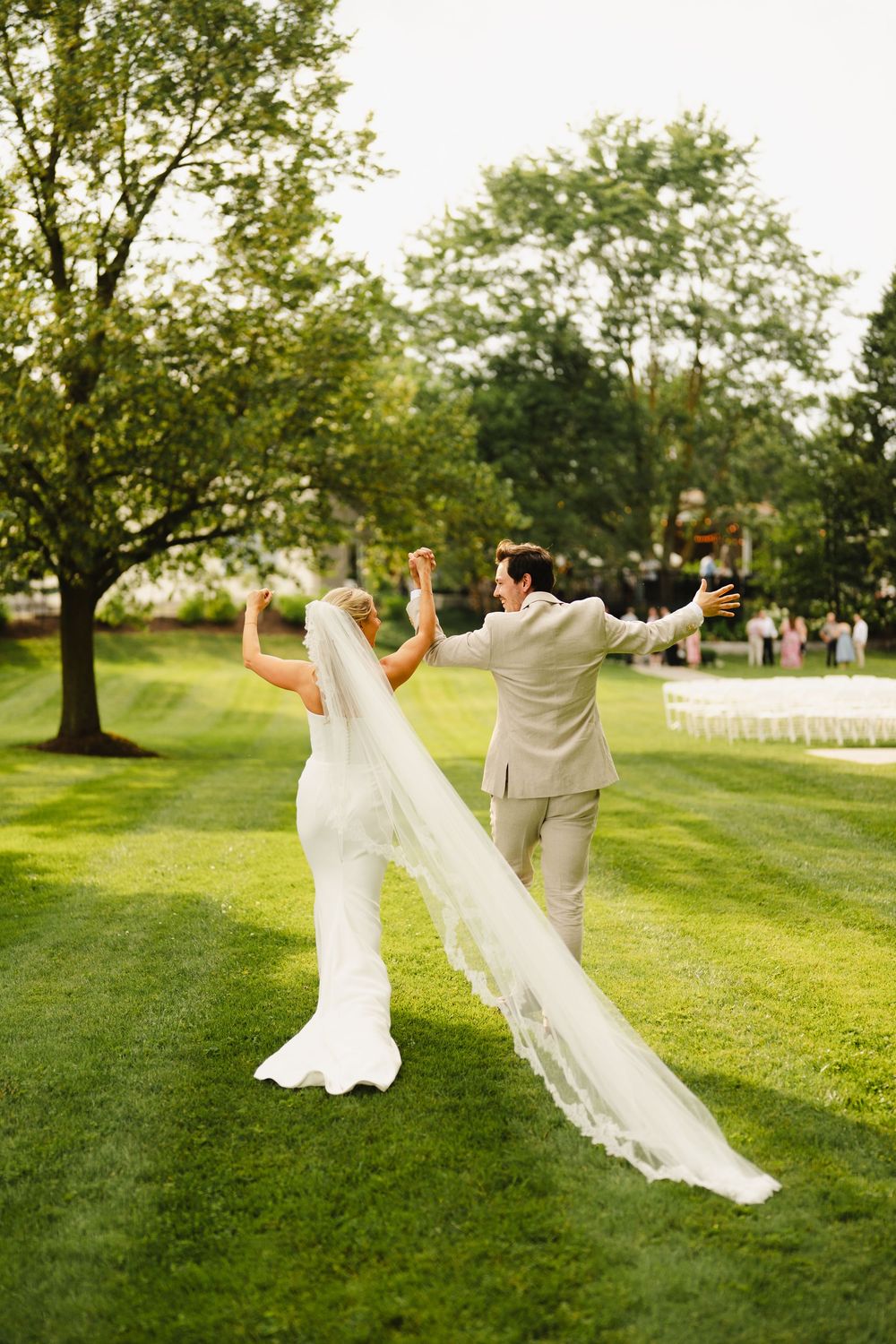 Playful wedding couple runs and jumps on a lush green lawn during golden hour photography session.