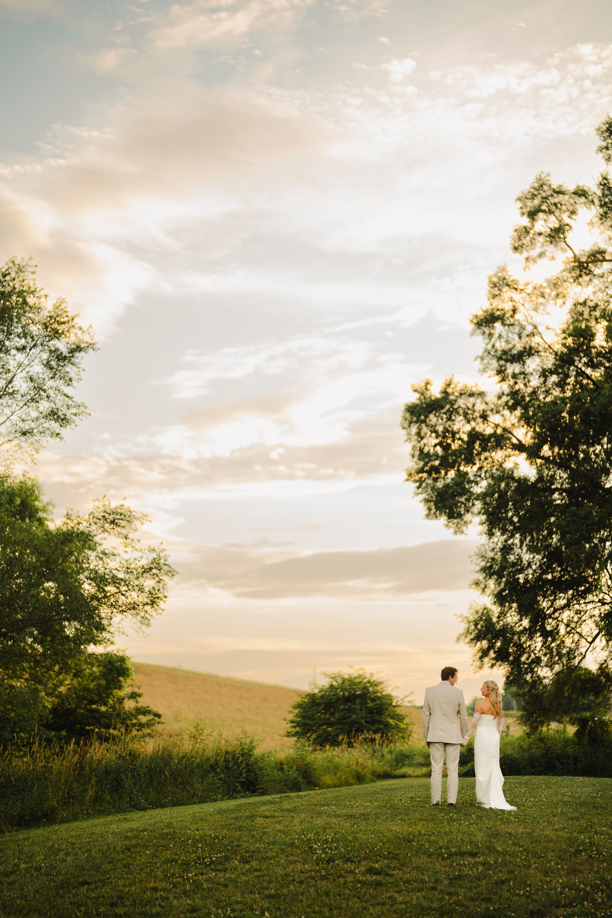 Silhouetted couple stands together on a hilltop during a dramatic sunset wedding photoshoot.