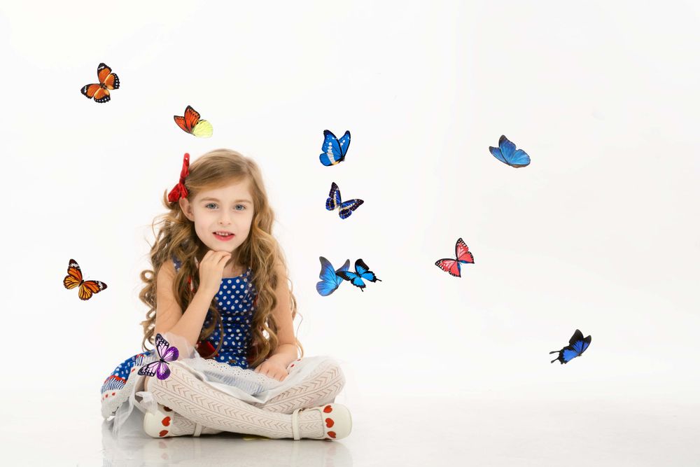 Child in polka dot dress sitting cross-legged on white background with colorful butterflies floating around.