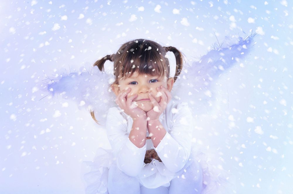 A small child in white clothing giggles with delight while snowflakes fall around them.