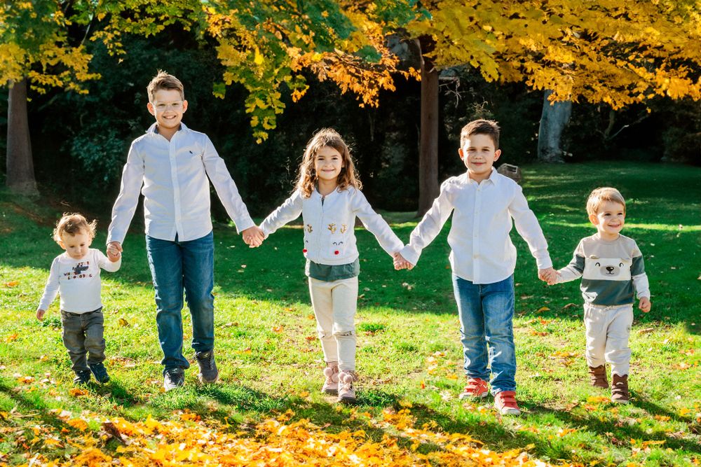 Five people walking hand in hand across a sunny autumn lawn with vibrant yellow leaves and trees in the background.