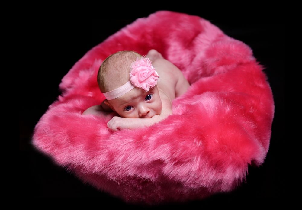 A sleeping newborn baby lies on soft pink fur with a matching pink headband.