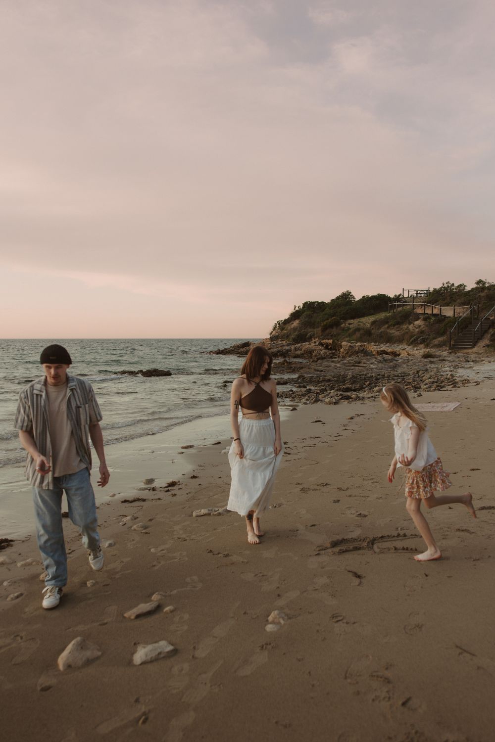 People walking along a rocky beach at sunset with cliffs in the background.
