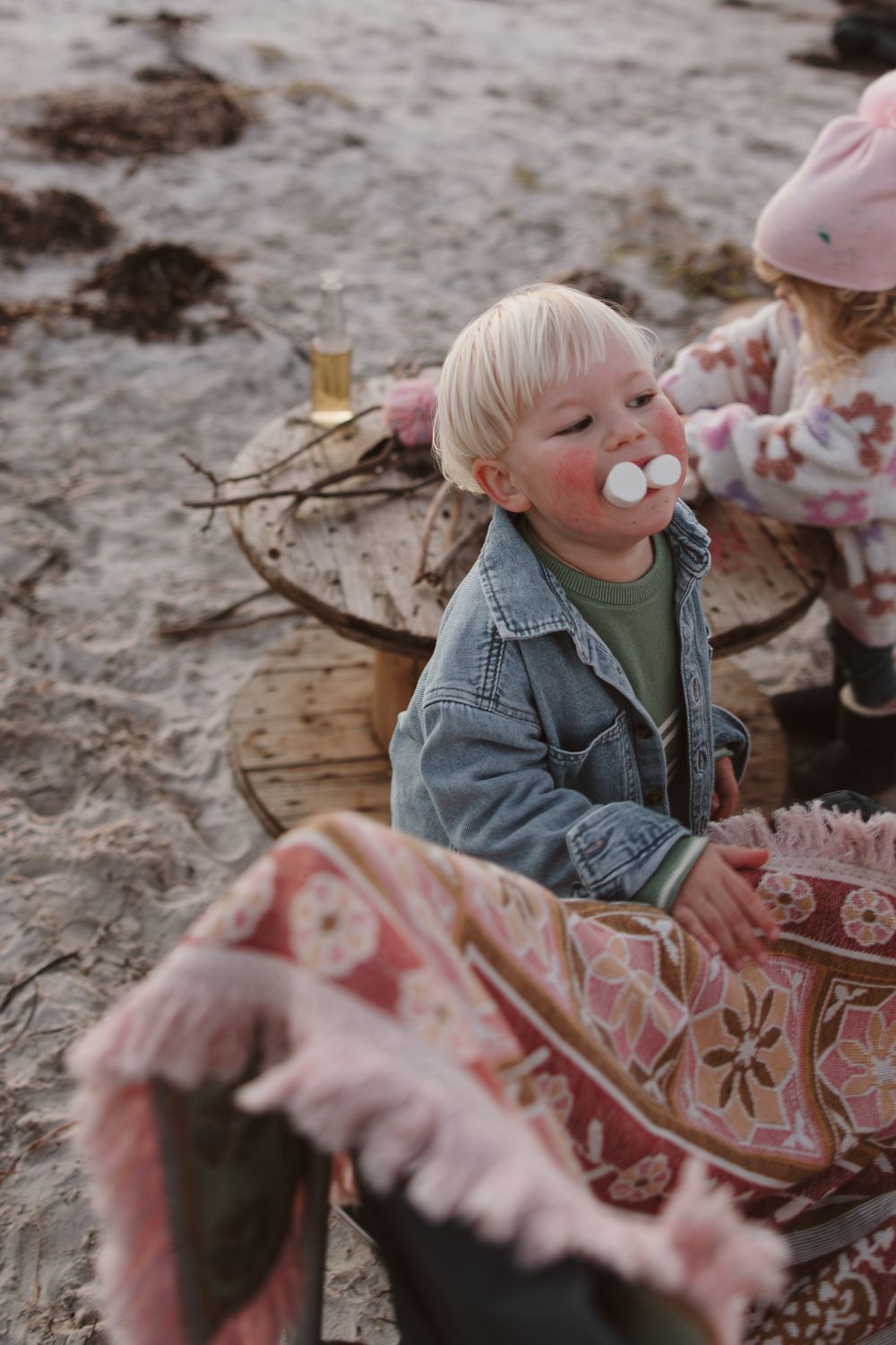 Child enjoying marshmallows while sitting on a cozy blanket at the beach.