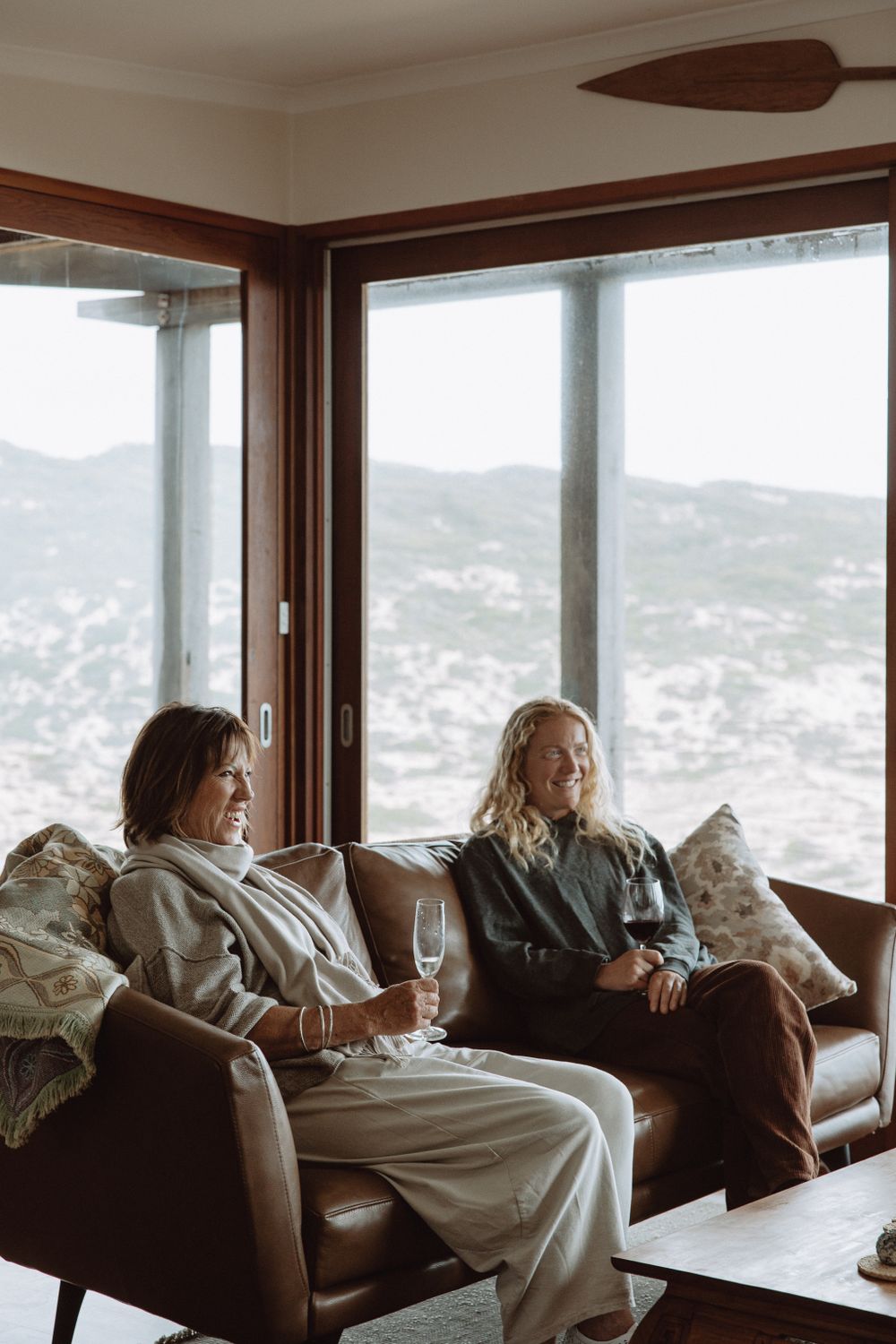 People relaxing on brown leather couches in a room with panoramic mountain views.