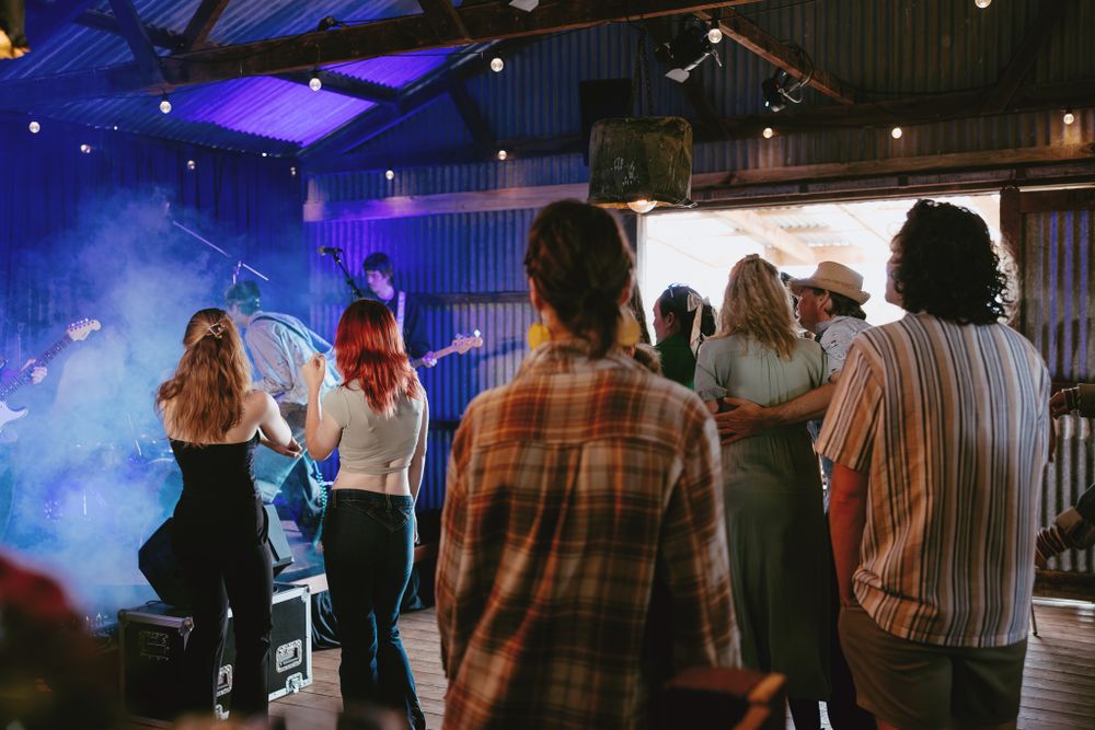 Concert audience silhouettes against blue stage lighting in a rustic venue.