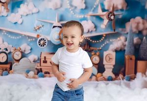 Child smiles in front of whimsical aviation themed backdrop with wooden toy airplanes and fluffy clouds.