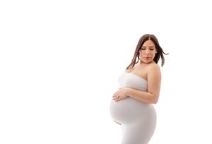 Pregnant woman in white dress cradling her baby bump against a white background.