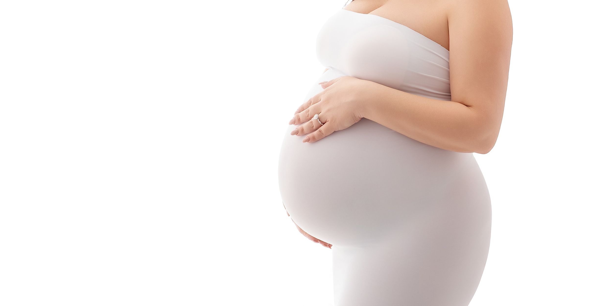 Pregnant woman in white dress cradling her baby bump against a white background.