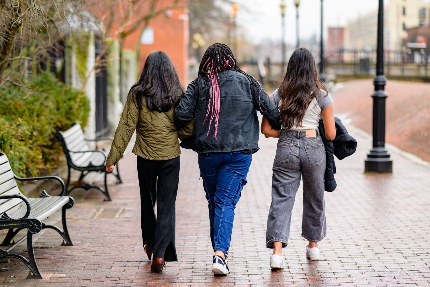 Three young women walking on brick pavement away from the camer in an urban setting,