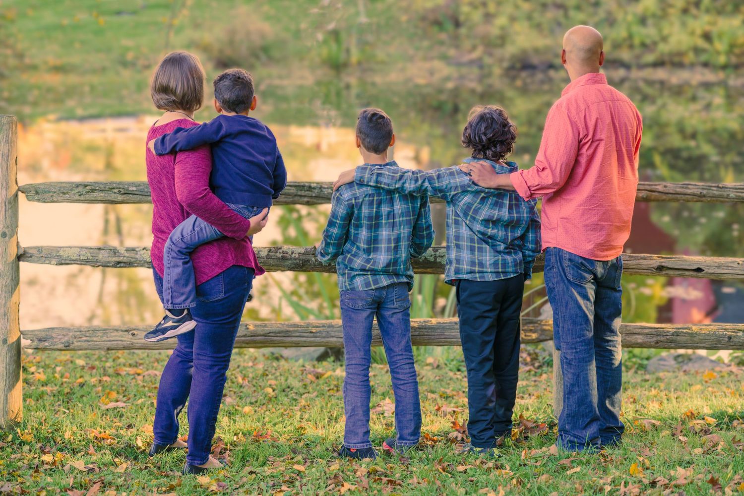 A family photography of a mother, father and three sons in autumn by at post and beam fence.