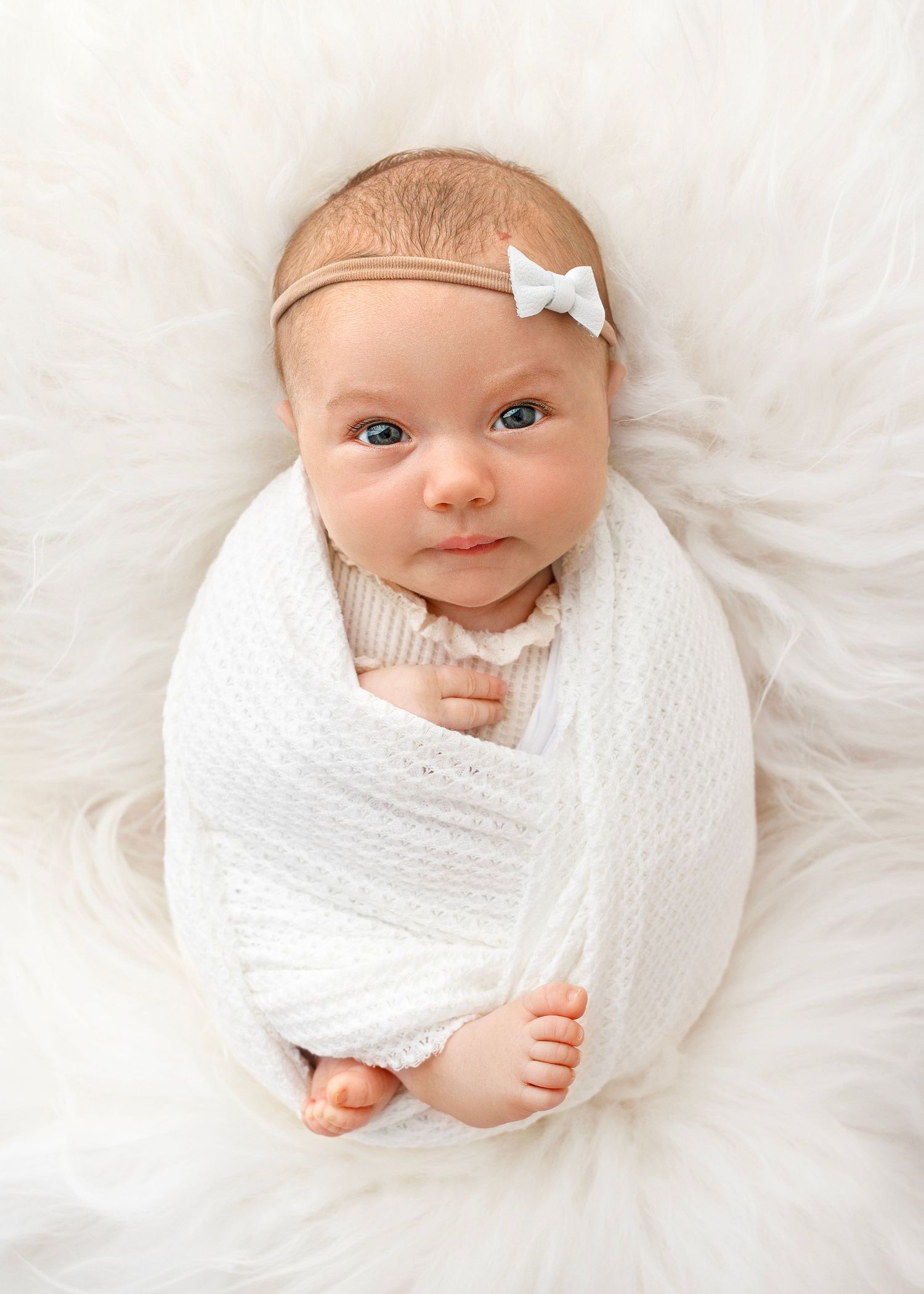 Bright eyed baby wrapped up snuggly and peering up with curiosity towards camera
