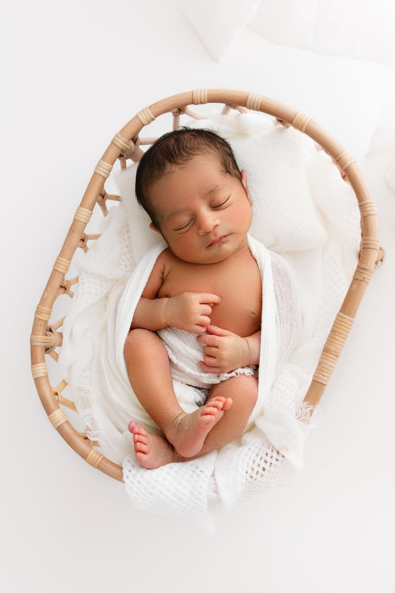 Baby boy sleeping peacefully in a tiny bassinet during his newborn photoshoot