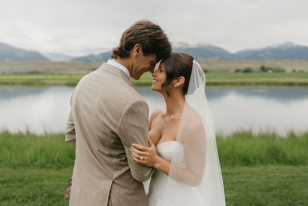 Newlyweds embracing in front of a serene lake and mountain landscape.