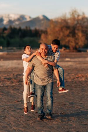 Three people playing and laughing together on a beach with mountains visible in the distance.