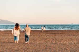 Two people walking along a sandy beach at sunset with mountains in the distance.