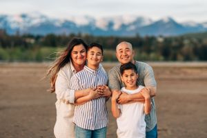 Family portrait on beach with snow-capped mountains in background during golden hour.
