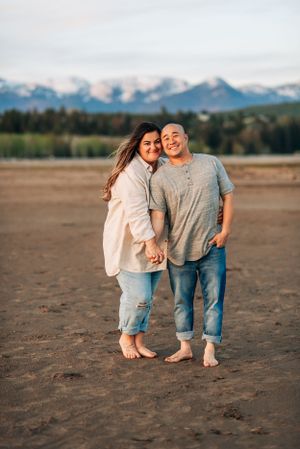 Couple sharing intimate moment on beach with mountain landscape behind them.