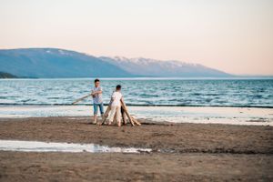 Two people standing on beach at sunset with mountains in background.
