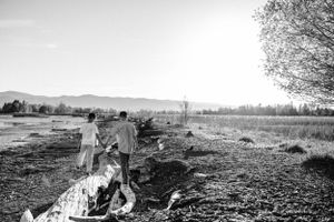 Black and white photo of a scenic landscape with people walking along a fallen log at sunset.