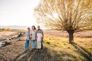 Family standing together on a dirt path near a large tree during golden hour.
