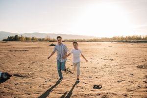 Two people playing and running together on a desert landscape at sunset.