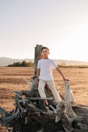 Person in white clothing posing on driftwood in desert landscape during sunset.