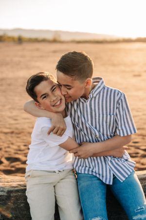 A tender moment shared between two people sitting on driftwood at golden hour in a desert setting.