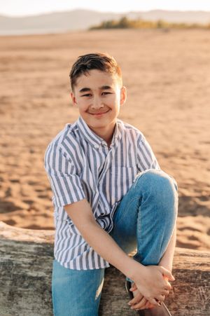 Person in striped shirt and jeans sitting casually on driftwood during golden hour.