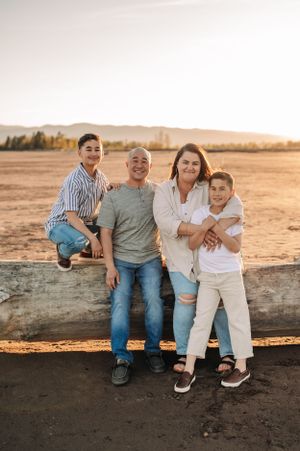 Family of four posing together on a fallen log during sunset in a desert landscape.