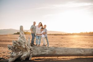 Family standing together on driftwood during golden hour with mountains in background.