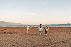 People walking along a beach at sunset with mountains in the distance.