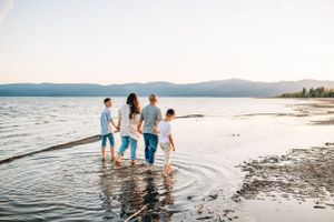A group enjoying a beach day splashing in the shallow water with mountains in the background.
