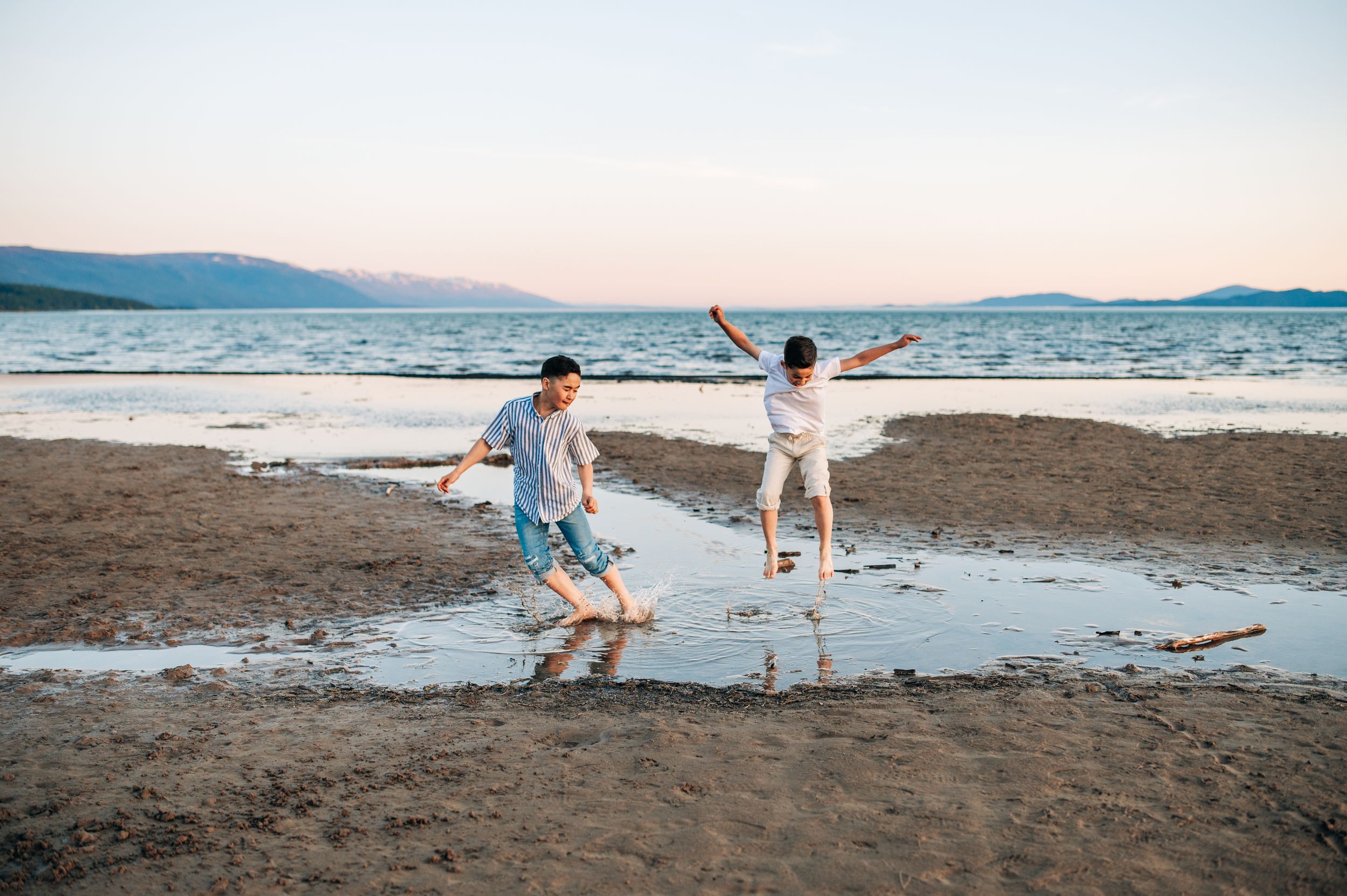 People playing and splashing in shallow water at a beach during sunset.