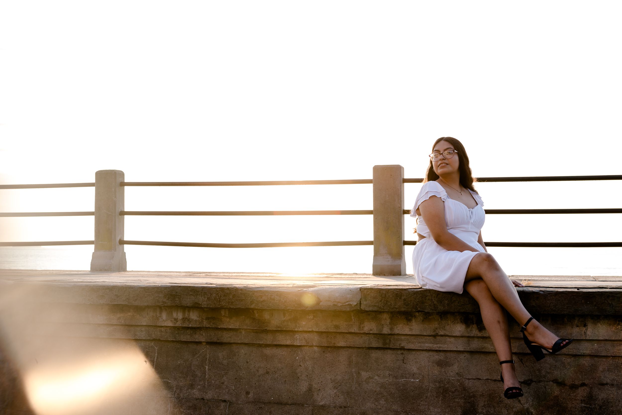 Charleston, Summerville,South Carolina. Woman in white dress sitting on stone railing at sunset, looking up peacefully at golden hour light.