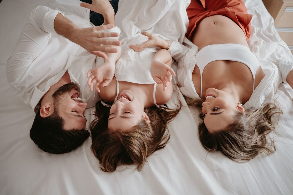 Happy family lying on white bed together, smiling and laughing in casual comfortable clothing.