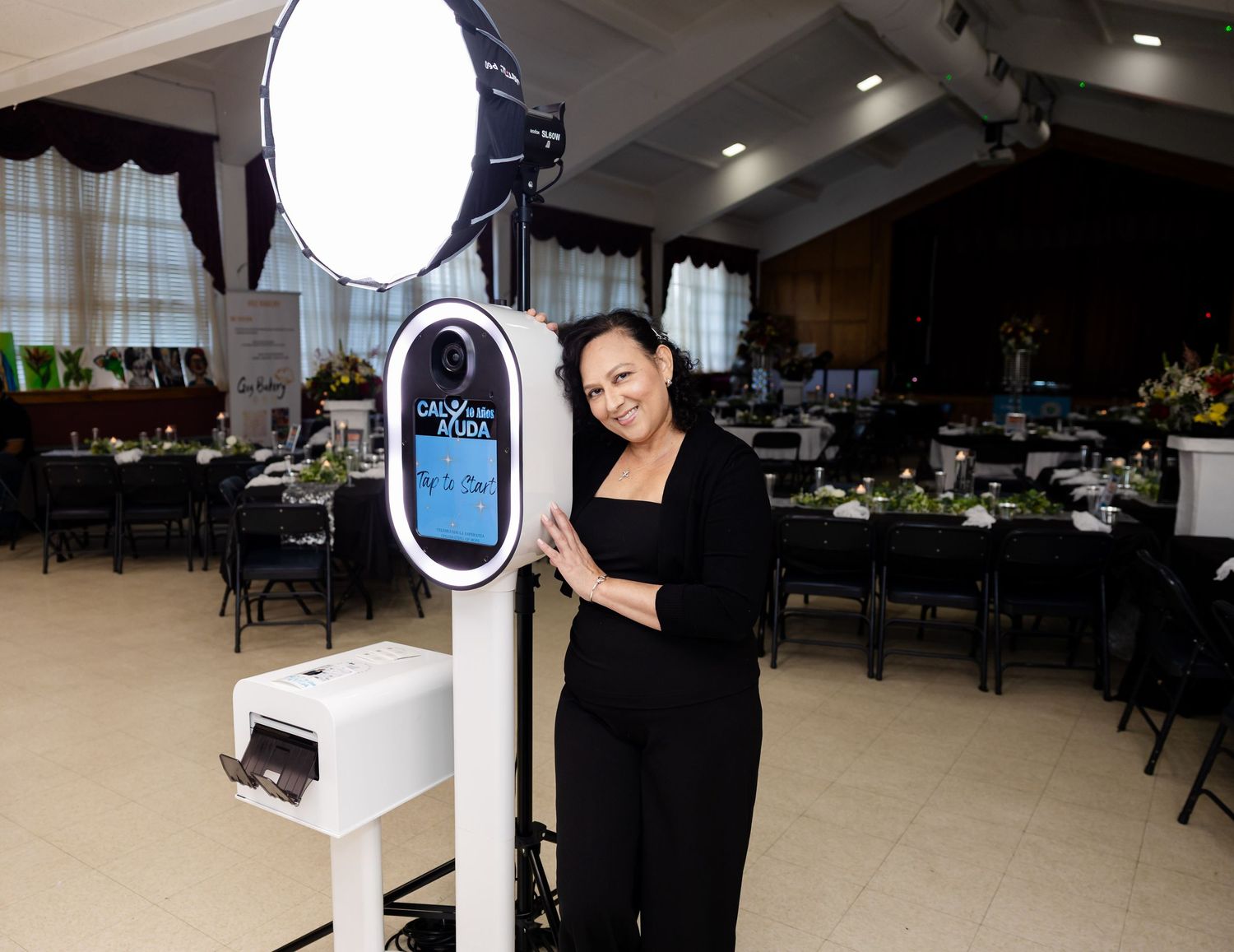 A person in a black dress interacts with a white digital kiosk display in a restaurant setting.