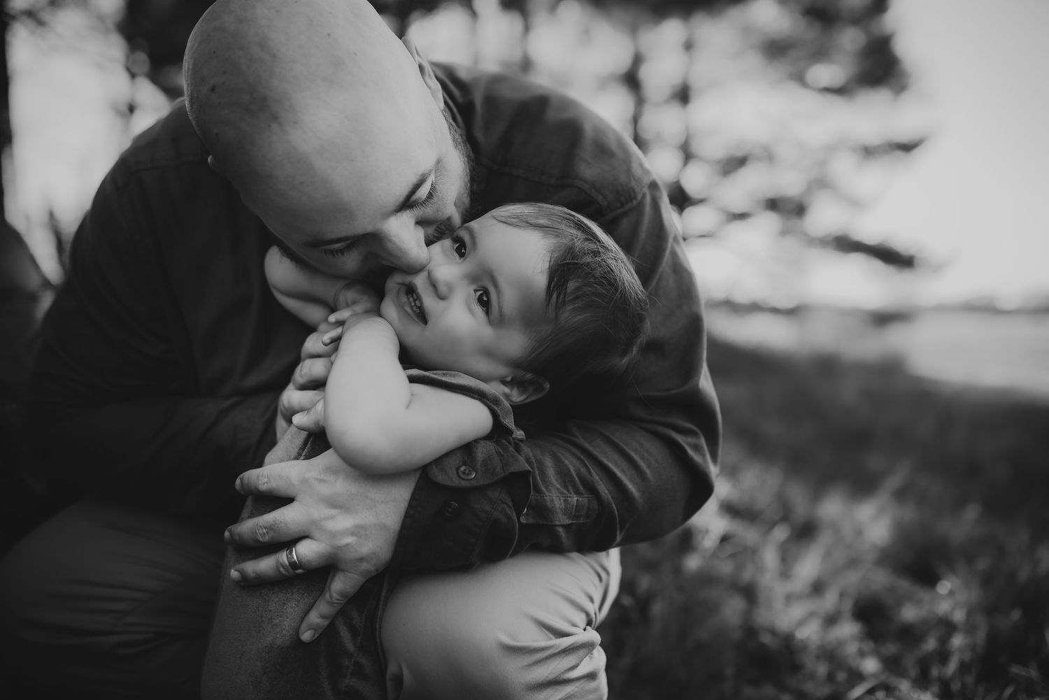 A tender black and white portrait of a parent embracing and kissing a young child outdoors.